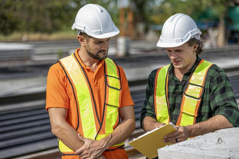 Dois técnicos de capacete e colete conferindo uma prancheta